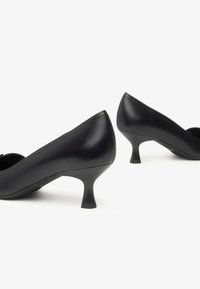 Black leather high-heeled shoes with rounded toes and a small, flared heel. Smooth texture and minimal design details.