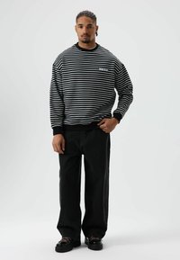 Sweat-shirt à rayures noires et blanches avec une coupe décontractée, accompagné d'un pantalon noir à jambes larges et de chaussures noires épaisses. Tissu lisse et poignets côtelés.