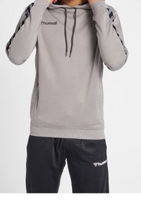 Sudadera gris con un diseño texturizado, cordones y acentos negros en los laterales. Combinada con pantalones negros que tienen un logo blanco en la pierna.