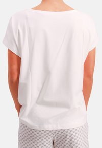 White short-sleeve blouse with a round neckline, smooth texture, and relaxed fit. Worn with patterned light-colored pants.