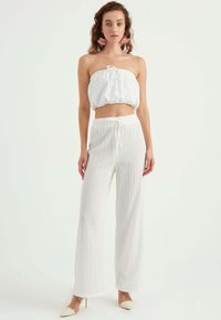 Vit tvådelad outfit bestående av en strapless crop top med knyt-detalj och vida byxor, båda i texturerad tyg. Neutrala klackar.