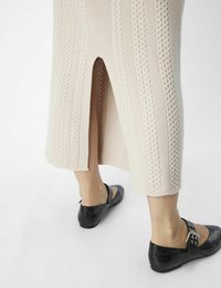 Stickad pennkjol i ljusbeige med texturerade kabelmönster och en bakslits; matchad med svarta texturerade ballerina-skor med spänne.