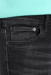 Mustad teksapüksid, millel on klassikaline lõige, ees tasku nööpkinnitusega ja peen tekstuur. Kandmiseks koos mintrohelise topiga.