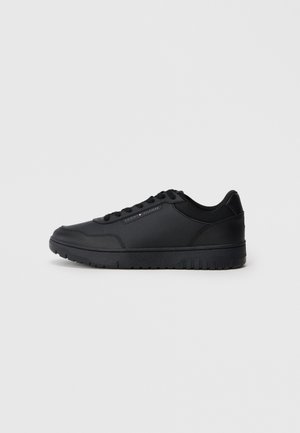 Zapatilla deportiva negra de material sintético suave, punta redonda, acentos perforados, diseño con cordones y suela de goma texturizada.