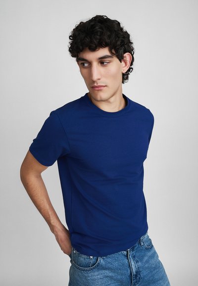 Dunkelblaues Kurzarm-T-Shirt aus leichtem, glattem Stoff. Schlichter Rundhalsausschnitt und taillierte Passform, kombiniert mit hellen Jeans.