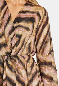 Langmesige wikkeljurk in een meerkleurig golvenpatroon met roze, bruin en gouden tinten. Lichtgewicht, gestructureerde stof met een vastgebonden taille.