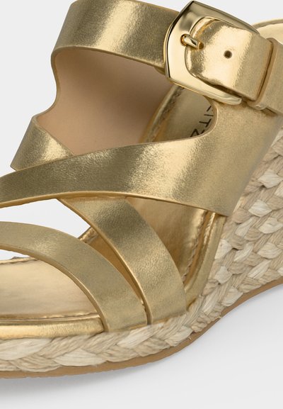 Sandale compensée métallique dorée avec brides croisées, boucle réglable et détail de semelle en corde tressée.