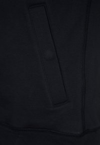 Tessuto di felpa nero con una texture liscia, dotato di una tasca laterale e cuciture a contrasto lungo le giunture.