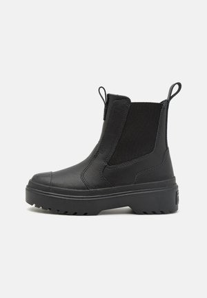 Botines negros de piel suave con paneles laterales elásticos, puntera redonda y suela de goma gruesa con un patrón de tracción.