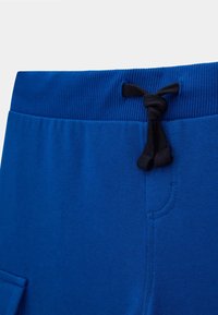 I pantaloni sportivi blu in cotone presentano un cinturino a costine, un laccio nero e una tasca laterale con una superficie liscia.
