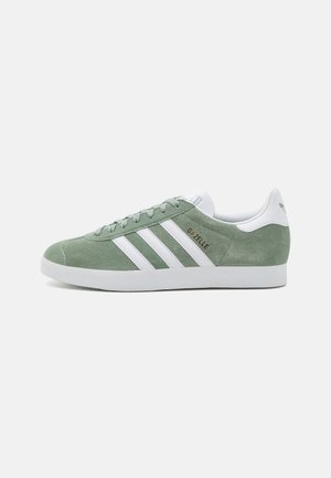 Lavprofil Adidas Gazelle sneaker i grøn ruskind med hvide striber, hvid hælkappe, snørebånd og gummisål, vist i sideprofil.