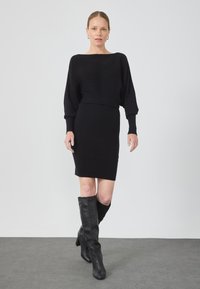 Rochie neagră din tricot cu model cu dungi, cu decolteu larg de tip bateau și mâneci lungi, asortată cu cizme negre din piele, până la genunchi. Textură netedă pe întreaga suprafață.