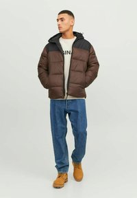 Pruun voodriga jakk musta kapuutsiga, millel on tõmblukk. Kanda kerge särgi ja siniste teksade peal, sobib hallide saapadega.