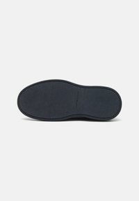 Suela de zapato de goma negra con acabado texturizado y sutil marca. Presenta una forma redondeada y una banda de rodadura con patrón para mejorar el agarre.