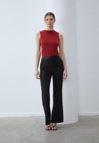 Top rojo sin mangas y pantalones de campana negros, diseño ajustado, textura suave, pantalones de corte slim, combinados con sandalias negras con tiras.