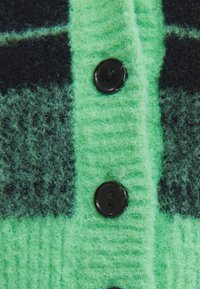 Zielony dzianinowy kardigan z czarnymi kratkowymi wzorami, teksturowaną tkaniną i trzema czarnymi guzikami na przedniej listwie.