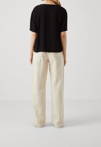 Haut noir à manches courtes avec col rond, associé à un pantalon large beige clair, offrant une coupe fluide et un tissu texturé.