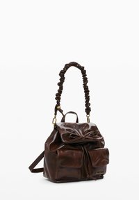 Pruun nahast käekott, millel on klapil kokku tõmmatud rihm ja lipsu detail, ning kaks esist kotti. Sile tekstuur kuldsete metalldetailidega.