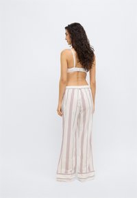 Λευκό σουτιέν με ρυθμιζόμενους ιμάντες σε συνδυασμό με παντελόνι με φαρδιά μπατζάκια που έχει κάθετες κόκκινες και μπλε ρίγες σε ανοιχτό υφασμάτινο φόντο.