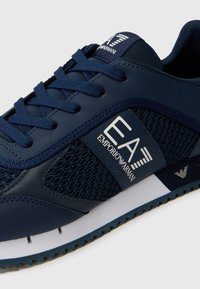 Navy sneaker with a combination of smooth and mesh materials, featuring a textured sole, laces, and a white logo accent.