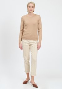 Maglione beige a maglia con scollatura e polsini a costine, abbinato a pantaloni color crema arrotolati e mule con tacco blocco marroni.