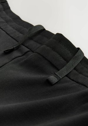 Pantalons de sport noirs avec une taille élastique, accents de cordon de serrage et tissu texturé. Un gros plan révèle des coutures et des détails de poche.