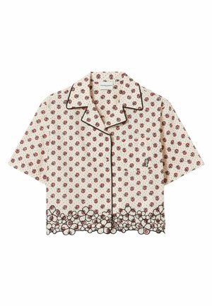 Le mannequin porte un haut crème à manches courtes boutonné et un short assorti avec un petit imprimé floral et un ourlet noir festonné, des mocassins marron, fond neutre.