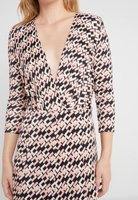 Vzorované šaty v černé, růžové a krémové barvě. Mají hluboký výstřih do V a tříčtvrteční rukávy. Materiál má hladkou texturu s geometrickým vzorem.