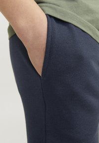 Marina blå bomullssweatpants med en sidoficka och en slät yta, kombinerat med en grön t-shirt som syns ovanpå.