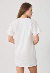 Fehér, rövid ujjú pamuting, egyenes szabású, látható varrási részletekkel az ujjakon és az alján.