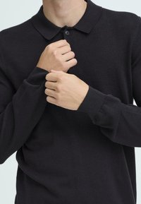 Sort langærmet polo skjorte med en klassisk krave, der har en knaplukning og ribbede manchetter. Blødt, tekstureret stof.