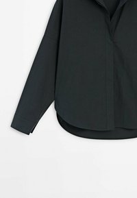 Chandail à manches longues gris foncé en tissu lisse, présentant une coupe décontractée, un ourlet arrondi et un col pointu. Détails de couture minimalement visibles.
