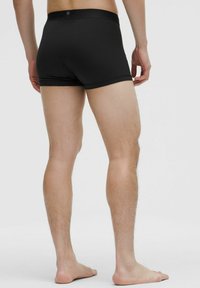 Melni bokseru šorti ar gludu audumu, elastīgu jostu un īsu kāju dizainu, atklājot ādu no vidukļa līdz pusceļam uz augšstilba.