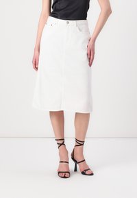 Hvit denim midi skjørt med rett snitt, front splitt og fem lommer, paret med svarte stroppehøyhælte sandaler.
