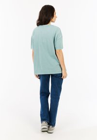 Lichtblauwe oversized t-shirt met korte mouwen, ronde halslijn en een gladde katoenen textuur, gecombineerd met blauwe spijkerbroek en grijze sneakers.