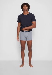 Grå boksershorts med svart midjebånd med «Levi's»-logo, kombinert med en enkel svart t-skjorte med korte ermer. Står barbeint.