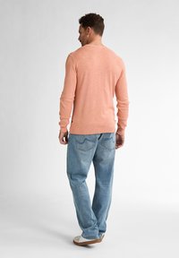 Helles rosa Langarmpullover mit gerippten Bündchen, kombiniert mit hellblauen Jeans mit Gesäßtaschen. Legere Schuhe runden das Outfit ab.