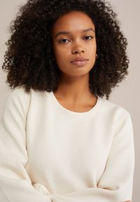 Krémová mikina s okrúhlym výstrihom, vyrobená z jemnej tkaniny. Voľné rukávy majú subtilnú textúru a detaily šitia.