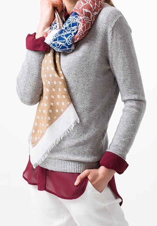 Pull gris avec bordure bordeaux, superposé à un chemisier bordeaux transparent. Une écharpe à motifs présente des tons bleus, rouges et marron avec des bords frangés.