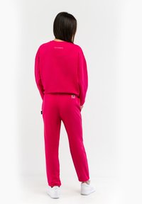 Pink sweatshirt and matching joggers made of soft fabric, featuring a loose fit, ribbed cuffs, and brand logo detail on the back.