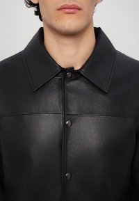 Black leather jacket featuring a large collar, snap button closure, and smooth texture with subtle stitching details.