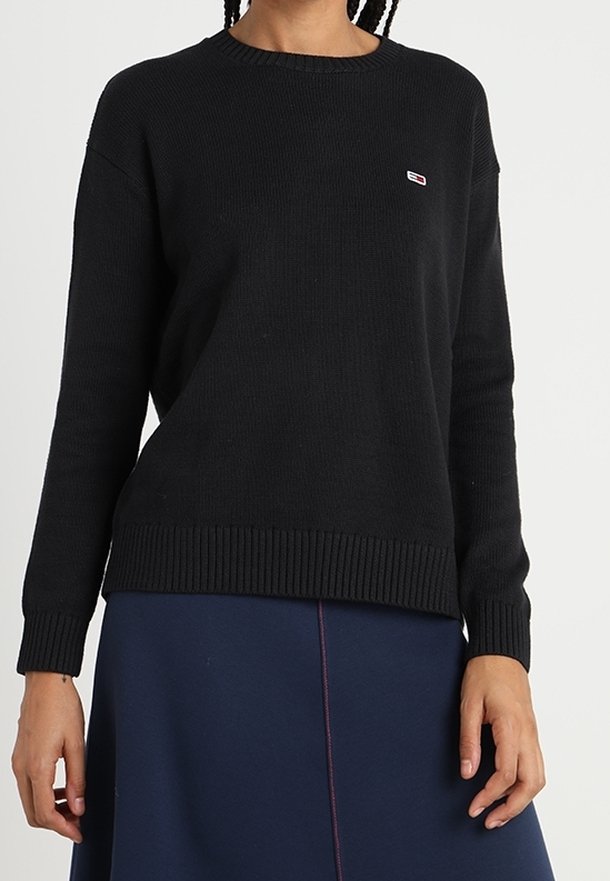 Pull noir en maille avec un col rond et des poignets côtelés. Présente un petit écusson logo sur la poitrine. Coupe ample avec une surface texturée.