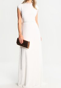 Witte maxi-jurk met korte kant sleeves, aansluitende taille en vloeiende rok. Gecombineerd met een rechthoekige bruine clutch.