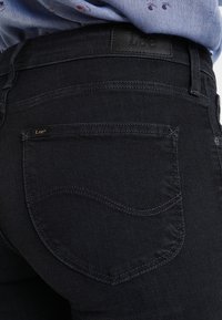 Vaqueros de mezclilla de lavado oscuro con una textura suave, que cuentan con un diseño en el bolsillo trasero y una etiqueta de cuero en la cinturilla.