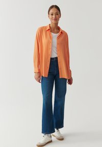 Orange button-up shirt, white t-shirt, and blue flared jeans. White sneakers with tan soles. Smooth fabric and casual fit.