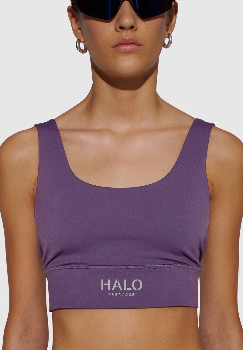 Lila crop top sportbh med fyrkantig halsringning och breda axelband. Har en silverfärgad "HALO"-logotyp nära nederkanten. Slät, elastisk tyg.