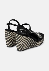 Sandali con zeppa in suede nero, con tacco intrecciato a righe e dettagli in strass sulla fascia, dotati di chiusura alla caviglia con fibbia.