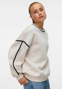 Lysegrå genser med svarte detaljer, med rund hals og puffede ermer. Laget av mykt materiale, den har en avslappet passform.