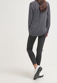 Svart och vit mönstrad långärmad skjorta, matchad med slitna svarta skinny jeans och vita platåskor.