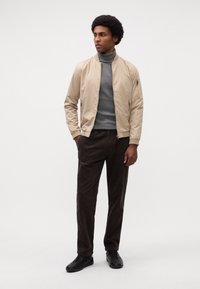 Beige bomber dzseki cipzáras zsebekkel, szürke garbó, barna kordbársony nadrág és fekete sportcipő. Simább anyag és slim fit szabás.
